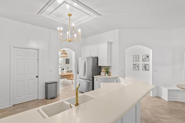 kitchen featuring freestanding refrigerator, arched walkways, white cabinets, a chandelier, and light countertops