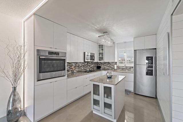 kitchen with glass insert cabinets, decorative backsplash, appliances with stainless steel finishes, white cabinets, and modern cabinets