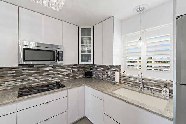 kitchen featuring decorative backsplash, white cabinets, a sink, appliances with stainless steel finishes, and a notable chandelier