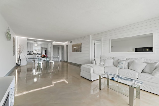 living room featuring wood walls, finished concrete floors, and baseboards