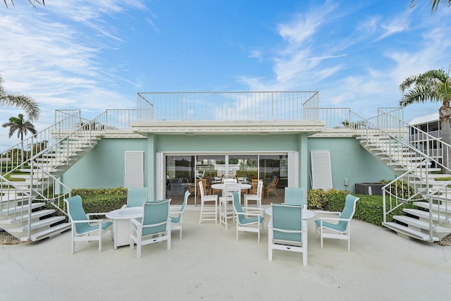 rear view of house with stucco siding, stairway, a patio, and outdoor dining area
