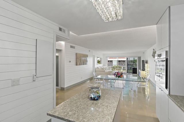 kitchen featuring a chandelier, oven, wood walls, light stone counters, and open floor plan