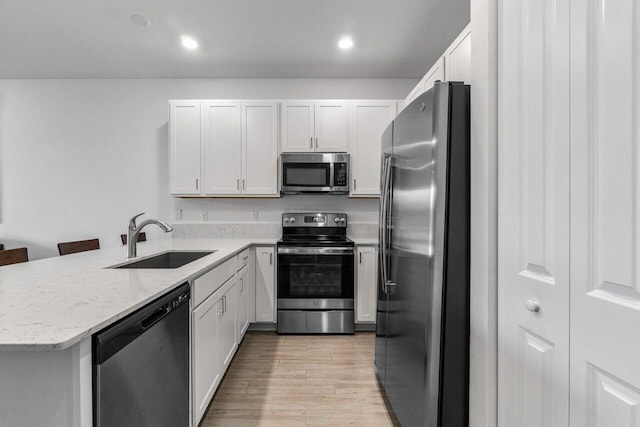 7113 Peters Ln, Delray Beach, FL 33446 - kitchen with a peninsula, appliances with stainless steel finishes, a sink, light wood-type flooring, and light stone counters
