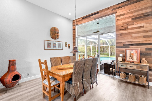 dining room featuring baseboards, a sunroom, vaulted ceiling, wood finished floors, and wood walls