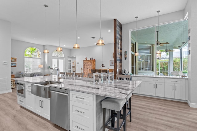 kitchen with stainless steel appliances, an island with sink, light wood-style flooring, and a sink