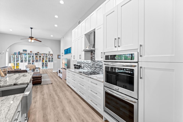 kitchen featuring arched walkways, wall chimney range hood, recessed lighting, black electric stovetop, and stainless steel double oven