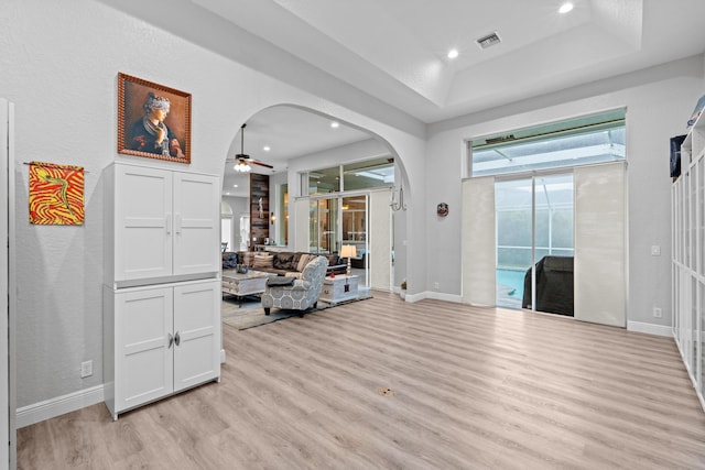 interior space with visible vents, a raised ceiling, arched walkways, ceiling fan, and light wood-style flooring
