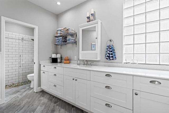 bathroom featuring a tile shower, wood finished floors, vanity, and toilet