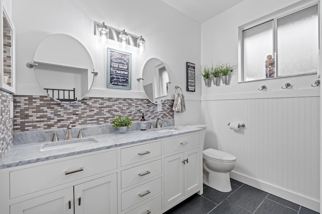 bathroom with a sink, toilet, double vanity, and a wainscoted wall