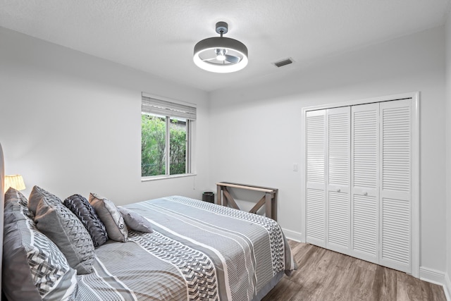 bedroom with a closet, visible vents, baseboards, and wood finished floors