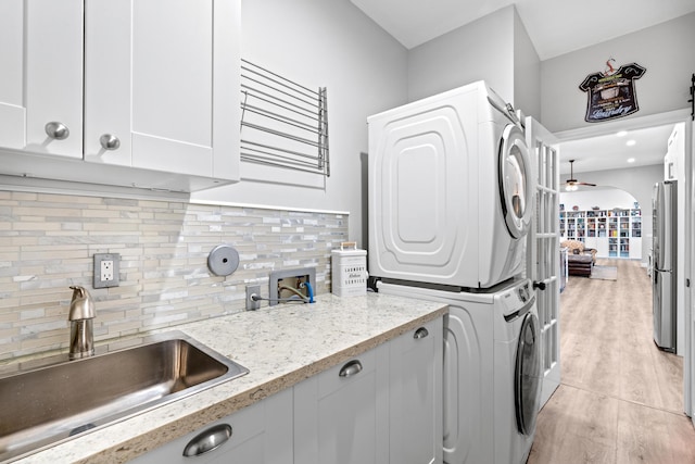 laundry area featuring a sink, a ceiling fan, stacked washing maching and dryer, cabinet space, and light wood-style flooring
