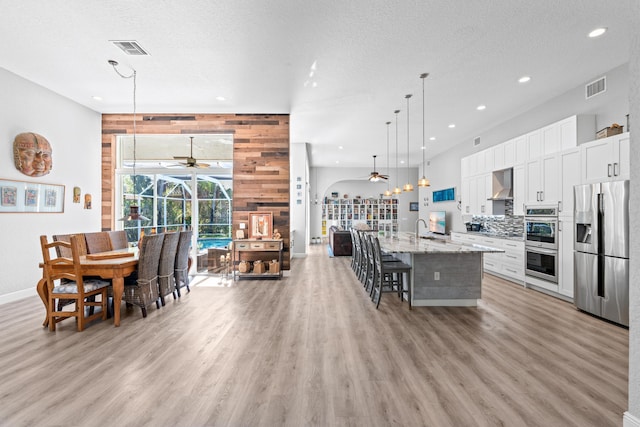 interior space featuring wall chimney range hood, appliances with stainless steel finishes, visible vents, and a ceiling fan