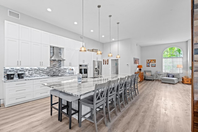 kitchen with visible vents, light wood-type flooring, stainless steel fridge, and wall chimney exhaust hood