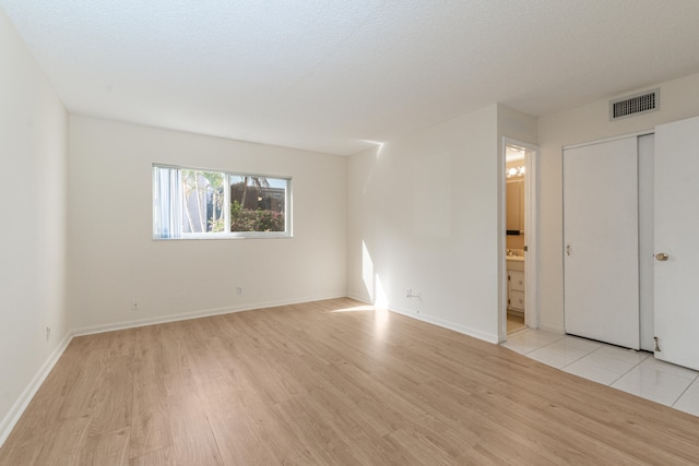 230 NE 26th Ave Unit 1030, Boynton Beach, FL 33435 - unfurnished bedroom featuring baseboards, connected bathroom, visible vents, and light wood-style floors