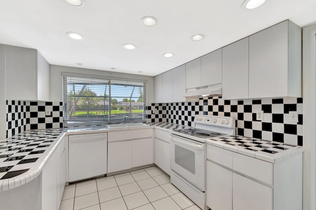 1746 W Terrace Dr, Lake Worth, FL 33460 - kitchen with white appliances, tile countertops, under cabinet range hood, decorative backsplash, and a sink