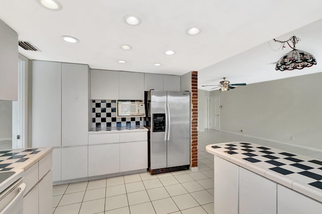 1746 W Terrace Dr, Lake Worth, FL 33460 - kitchen featuring stainless steel refrigerator with ice dispenser, tile counters, white microwave, a ceiling fan, and backsplash