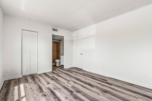 unfurnished bedroom with wood finished floors, a textured ceiling, ensuite bath, baseboards, and visible vents
