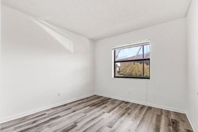 empty room with baseboards, a textured ceiling, and light wood-style floors
