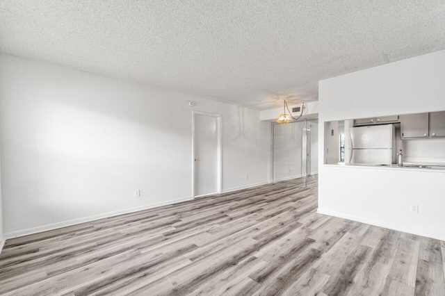 unfurnished living room with light wood-style flooring, a sink, a chandelier, and a textured ceiling