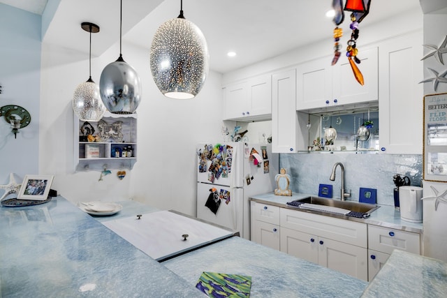 kitchen featuring white cabinets, decorative backsplash, freestanding refrigerator, and a sink