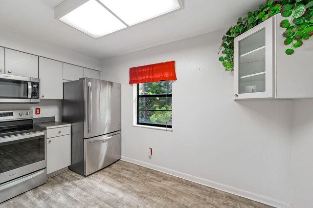 2050 Oleander Blvd Unit 3-206, Fort Pierce, FL 34950 - kitchen with appliances with stainless steel finishes, white cabinets, light wood-style flooring, baseboards, and glass insert cabinets