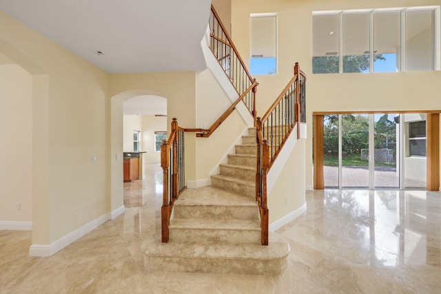 9682 Campi Dr, Lake Worth, FL 33467 - stairway featuring arched walkways, baseboards, marble finish floor, and a towering ceiling