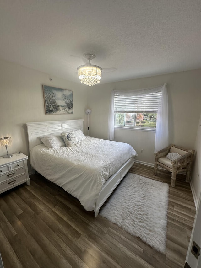 bedroom with dark wood finished floors, a textured ceiling, baseboards, and a chandelier