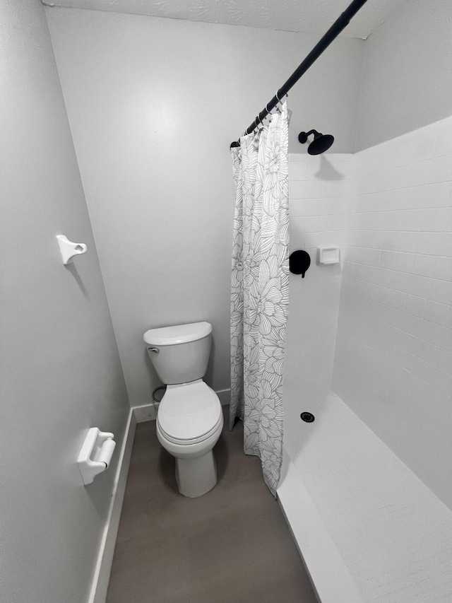 full bathroom featuring baseboards, toilet, a tile shower, and wood finished floors