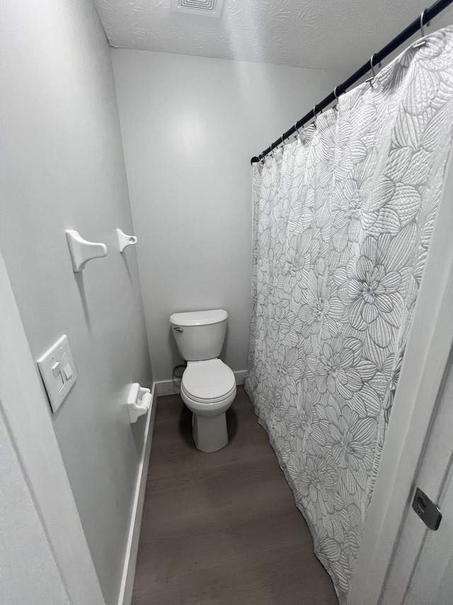 bathroom with toilet, wood finished floors, baseboards, and a textured ceiling