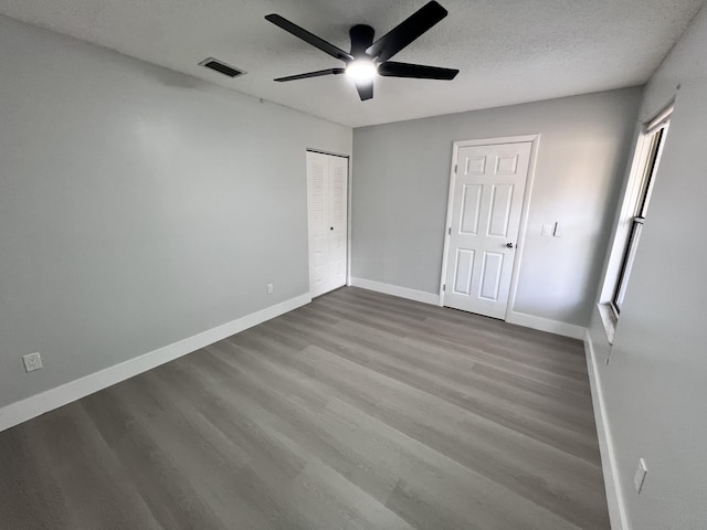 unfurnished bedroom featuring a textured ceiling, visible vents, baseboards, wood finished floors, and a ceiling fan