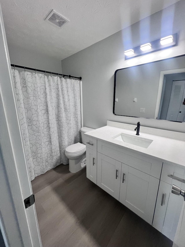 full bath with vanity, toilet, a textured ceiling, visible vents, and wood finished floors