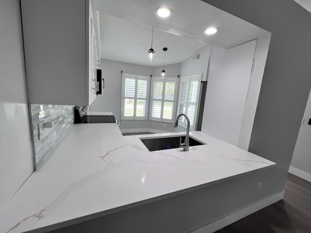 kitchen featuring a peninsula, appliances with stainless steel finishes, a sink, light stone counters, and hanging light fixtures