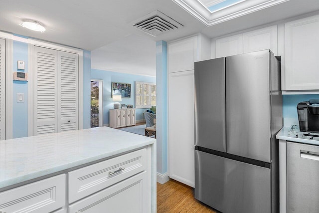 kitchen with light countertops, visible vents, white cabinets, light wood-type flooring, and freestanding refrigerator