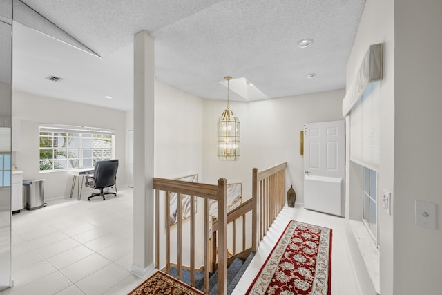 hallway featuring visible vents, baseboards, a chandelier, light tile patterned floors, and an upstairs landing