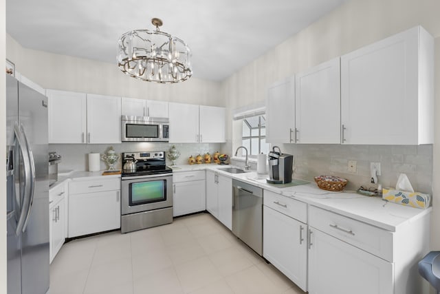 kitchen featuring white cabinetry, a sink, appliances with stainless steel finishes, backsplash, and a notable chandelier