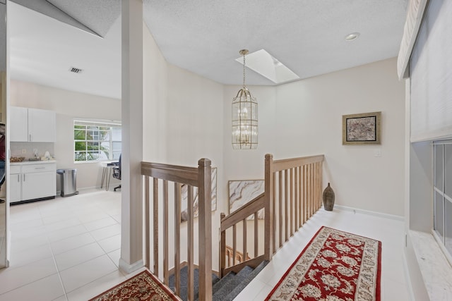 staircase featuring an inviting chandelier, visible vents, baseboards, tile patterned floors, and a skylight