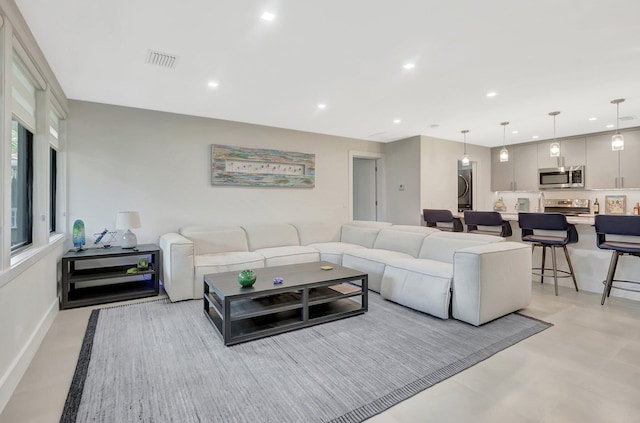 living area featuring stacked washer and dryer, concrete flooring, baseboards, visible vents, and recessed lighting