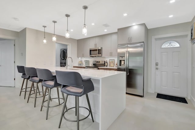 kitchen featuring stacked washer / drying machine, a kitchen bar, appliances with stainless steel finishes, gray cabinetry, and concrete flooring