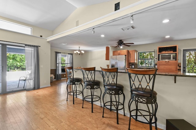kitchen featuring stainless steel appliances, a breakfast bar, a wealth of natural light, light wood-style flooring, and brown cabinets