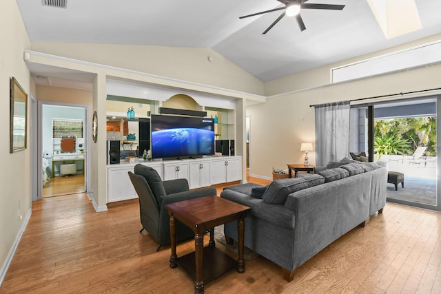 living room with a wealth of natural light, vaulted ceiling, a ceiling fan, and light wood-type flooring
