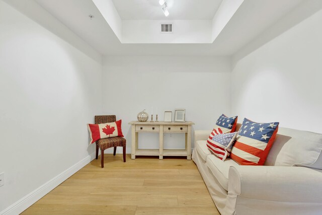 living area with visible vents, light wood-style flooring, track lighting, baseboards, and a raised ceiling