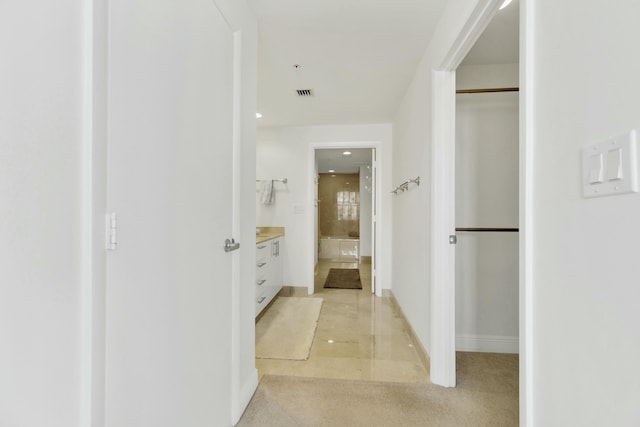 hallway featuring baseboards, visible vents, and light colored carpet