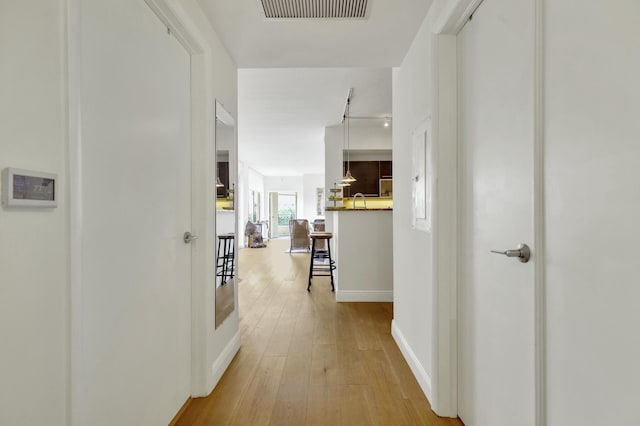 hall featuring light wood-style flooring, baseboards, and visible vents