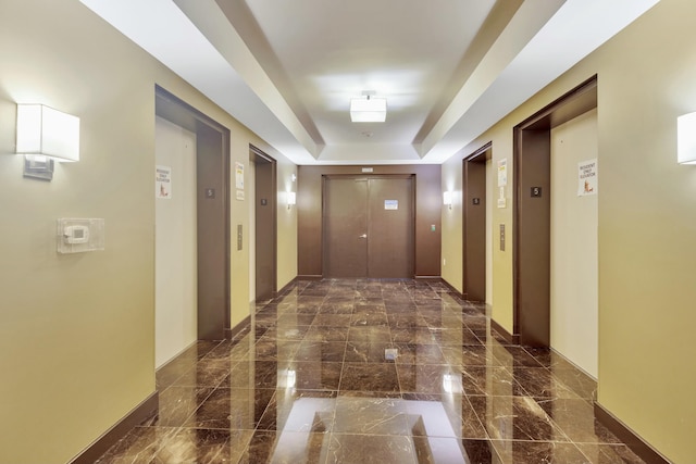 corridor with elevator, a tray ceiling, and baseboards