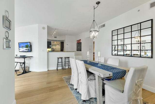 dining space featuring light wood finished floors, visible vents, rail lighting, and a chandelier