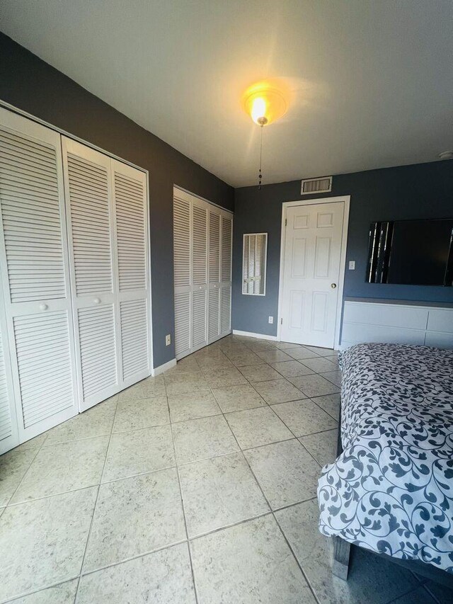 unfurnished bedroom with baseboards, multiple closets, visible vents, and light tile patterned floors