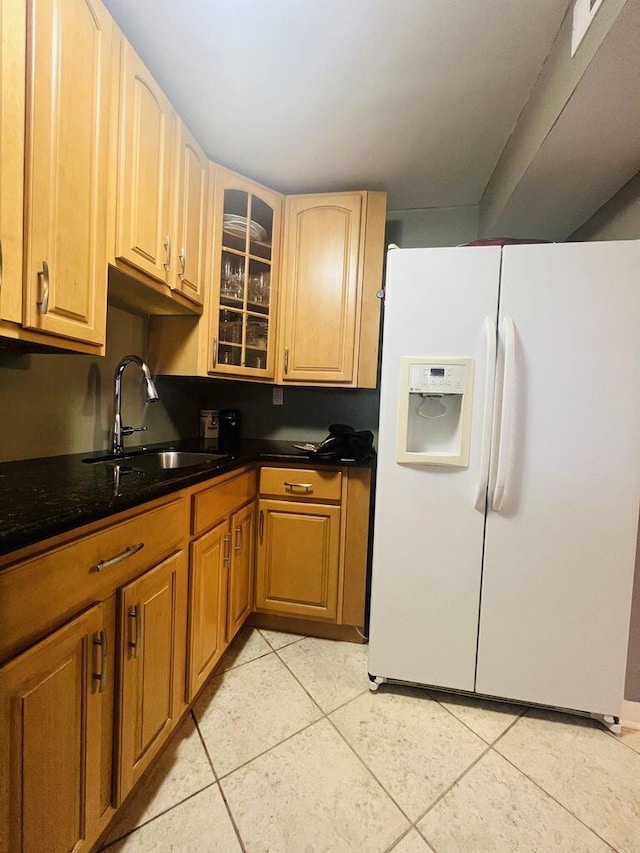 kitchen with glass insert cabinets, white refrigerator with ice dispenser, a sink, and light tile patterned flooring
