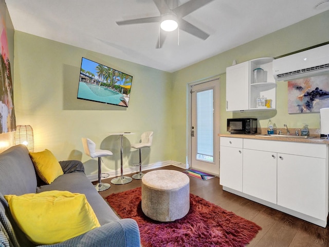 living area with baseboards, wood finished floors, a wall mounted air conditioner, and a ceiling fan