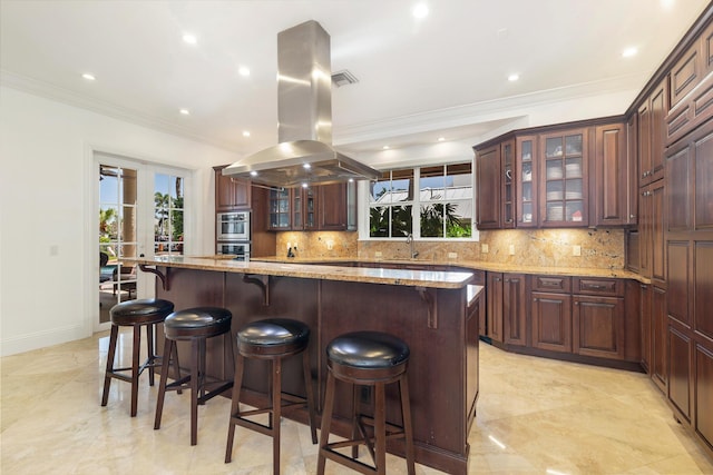 702 SE 7th St, Delray Beach, FL 33483 - kitchen featuring backsplash, island range hood, ornamental molding, a sink, and light stone countertops