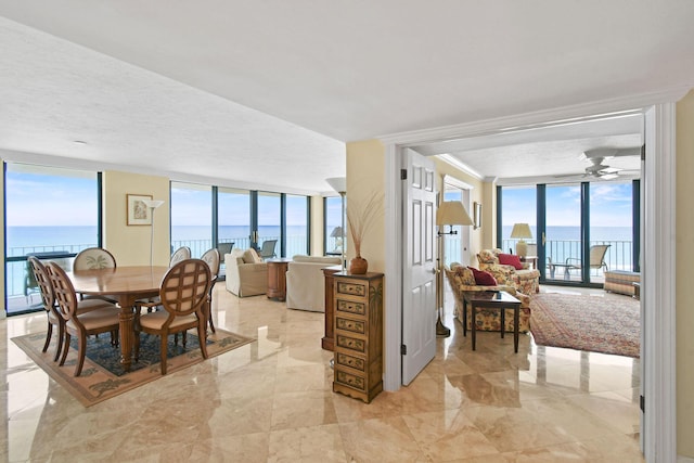 dining room featuring floor to ceiling windows, ceiling fan, a water view, and a healthy amount of sunlight